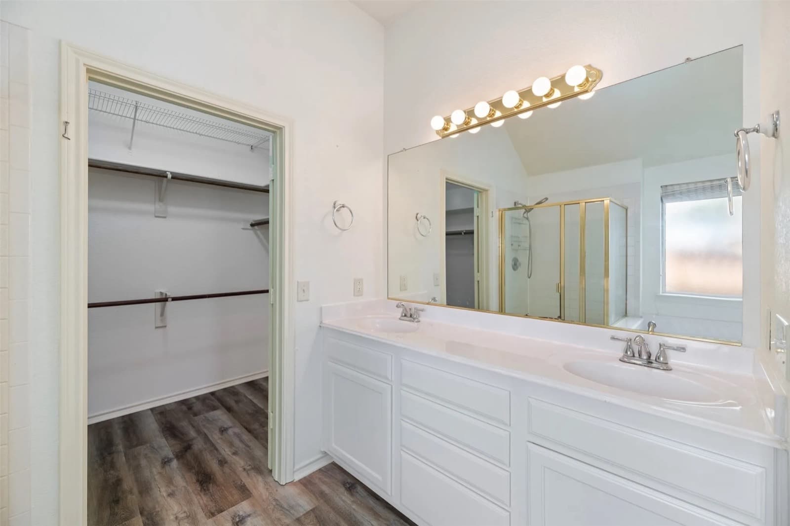 A rental bathroom with a white double vanity, a wide wall mirror, a bulb light bar and a walk-in closet.