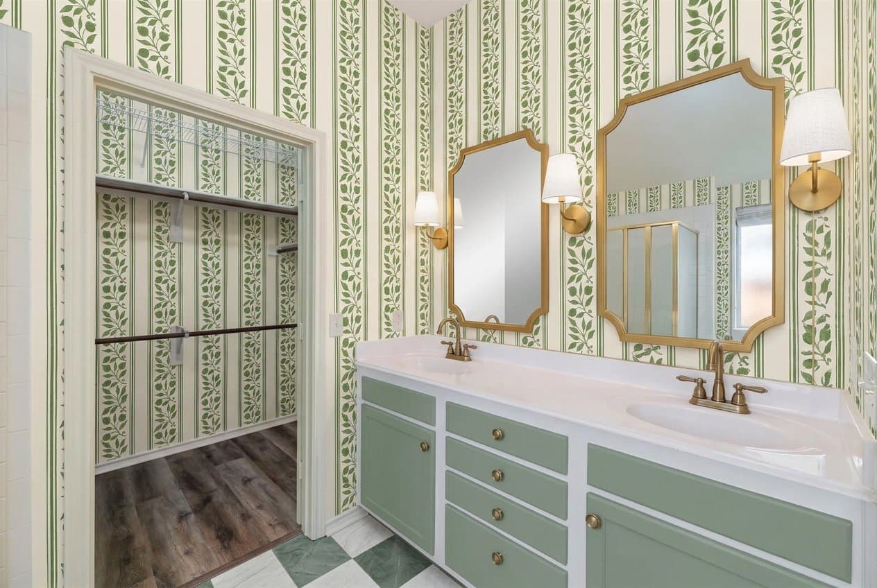 The same bathroom redesigned: leaf-stripe wallpaper, two gold mirrors with sconces, a sage vanity and a green checkerboard floor.